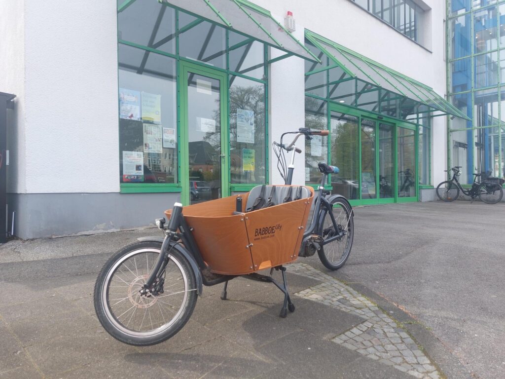 Ein Lastenrad in holländischer Optik mit hölzerner Ladebox, in der eine Sitzbank für Kinder montiert ist