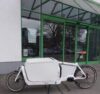 Ein ganz in weiß gehaltenes Lastenrad mit großer, rundum verschlossener Alubox auf der Ladefläche
