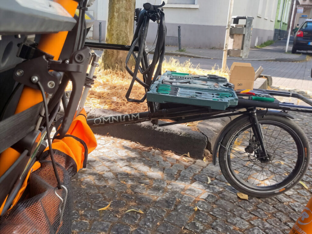 Ein Lastenrad mit einem Werkzeugkoffer auf der Ladefläche steht neben einer Rikscha